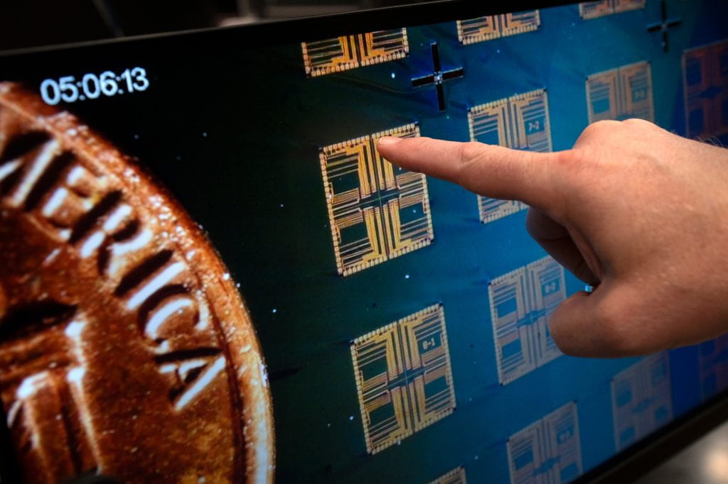 Peter Burke shows the sensor chips under a microscope with a penny included for scale. Steve Zylius / UC Irvine