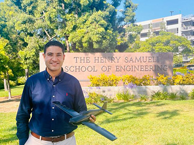Haithem Taha holding model airplane in front of Henry Samueli School of Engineering sign.