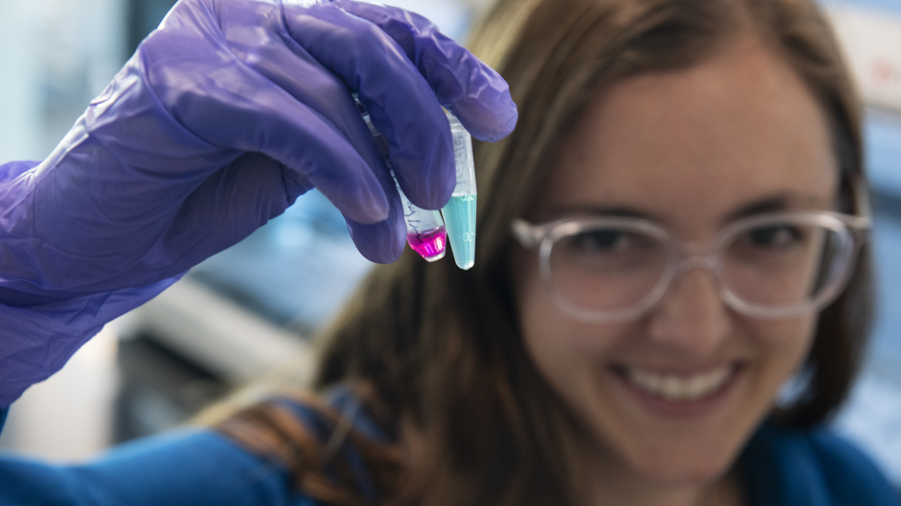 Female scientist holding up vial with colorful fluids.